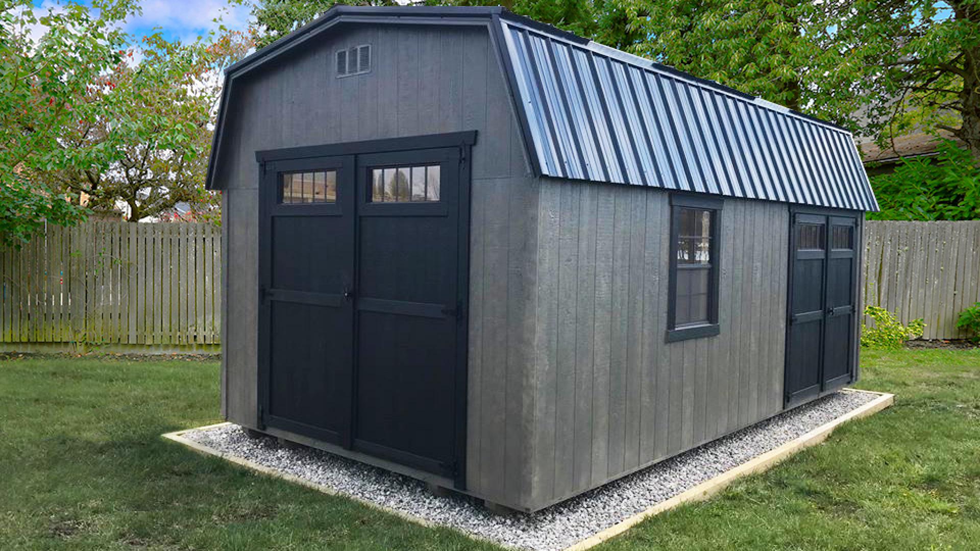 Signature high barn with grey wood siding, two sets of black double doors, black trim windows, and a black metal roof.