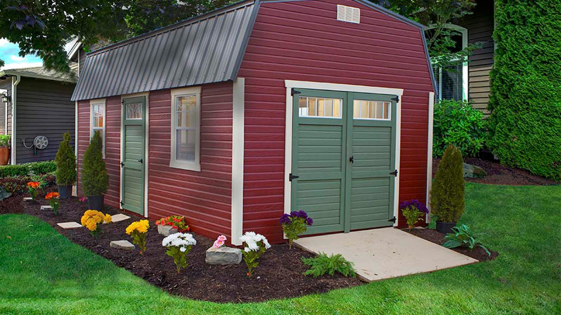 High barn with red siding, white trim, green double doors, windows, a green single door, and a metal roof sitting in a backyard.