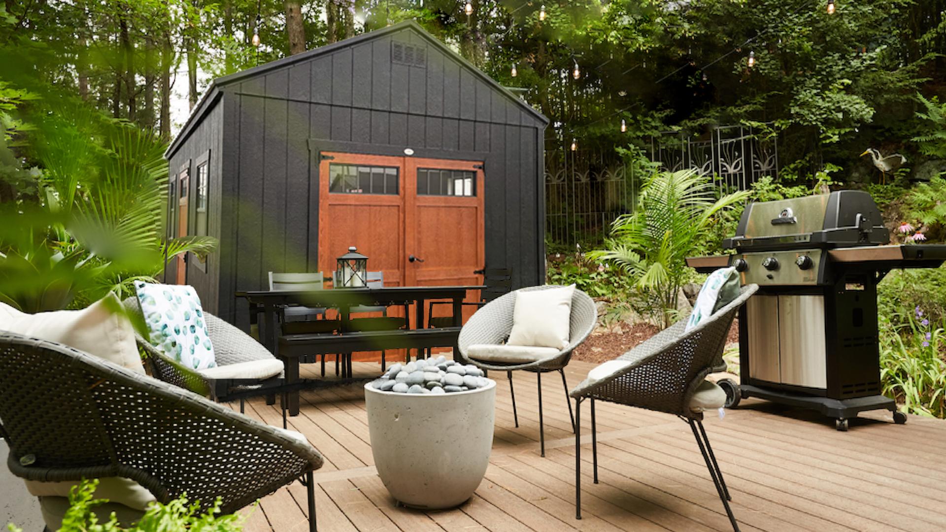 Compass Big Sky with black siding and brown double doors in a backyard with an outdoor table, grill, seating, and fire ring.